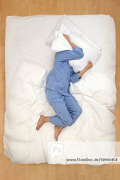Frau im Bett liegend mit Kissen über dem Kopf
