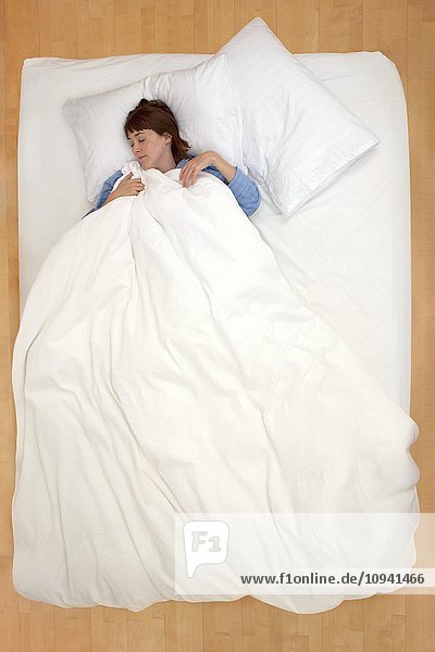 Frau liegt im Bett und hält die Bettdecke