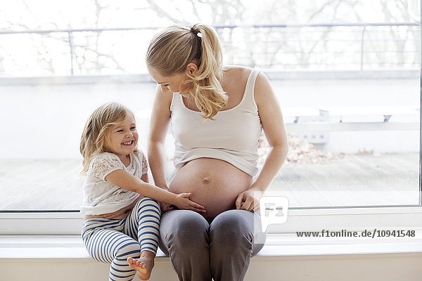 Mädchen berührt den Bauch der schwangeren Mutter