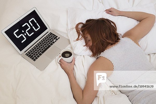 Erschöpfte Frau im Bett mit Laptop