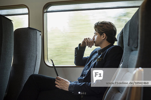 Side view of thoughtful businessman holding digital tablet in train