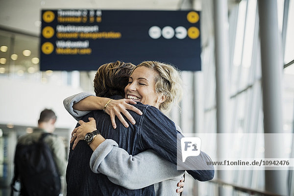 Glückliche Geschäftsfrau umarmt männlichen Kollegen am Flughafen