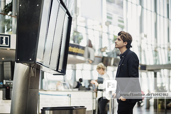 Geschäftsmann liest Ankunft Abfahrtstafel am Flughafen
