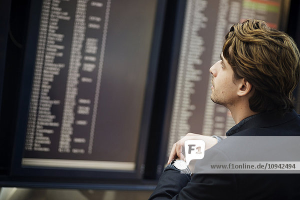 Geschäftsmann bei der Einstellung der Armbanduhr beim Lesen der Ankunftsanzeige am Flughafen