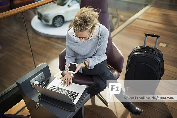 Hochwinkelansicht der Geschäftsfrau mit Laptop und Smartphone in der Flughafenlobby