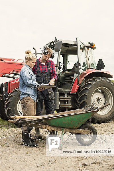 Frau und Mann diskutieren mit dem Traktor über ein Dokument auf dem Bauernhof.