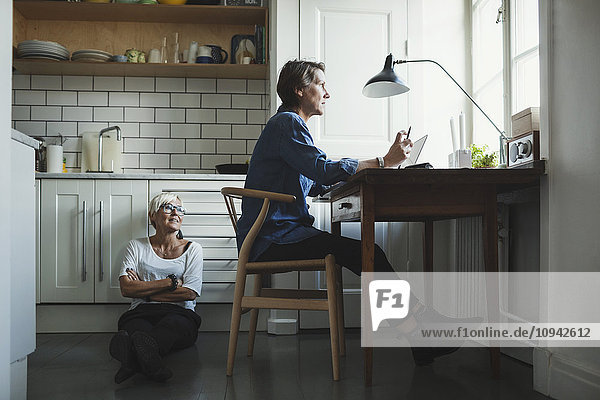 Female industrial designer looking at colleague while sitting on floor in kitchen