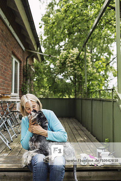 Fröhliche Seniorin küsst Hund auf der Veranda