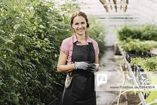 Portrait of smiling female gardener standing in greenhouse