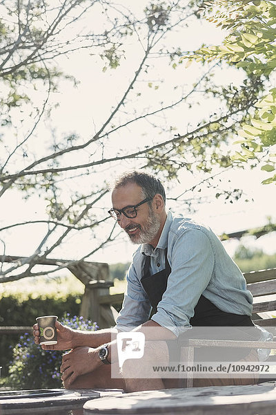 Glücklicher reifer Mann mit Kaffeetasse im Garten sitzend