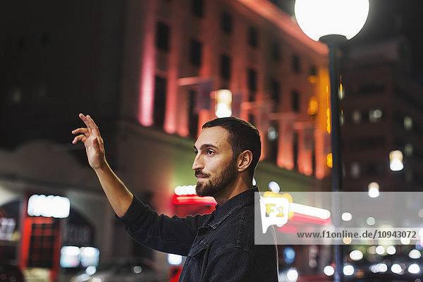 Seitenansicht eines jungen Mannes  der nachts in der Stadt ein Taxi ruft.