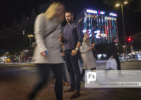 Volle Länge des Mannes mit dem Handy auf dem Bürgersteig in der Stadt in der Nacht