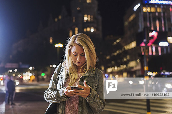 Woman using smart phone on city street at night