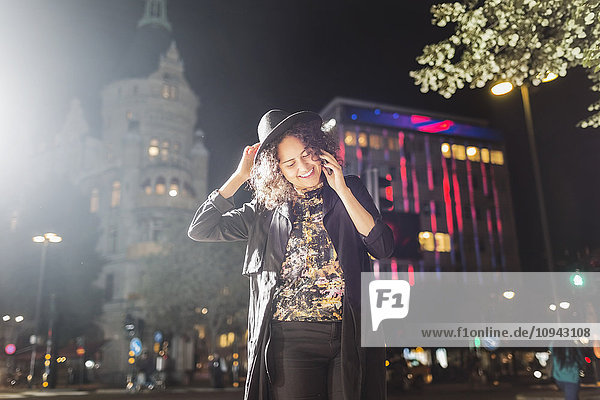 Lächelnde junge Frau  die nachts in der Stadt ans Smartphone geht.
