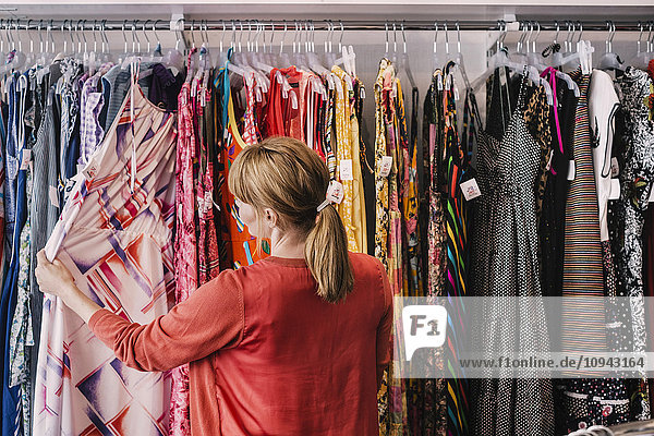 Frau schaut sich das Kleid an  das am Regal hängt  während sie im Laden steht.