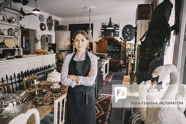 Portrait of female retailer with arms crossed standing in antique shop