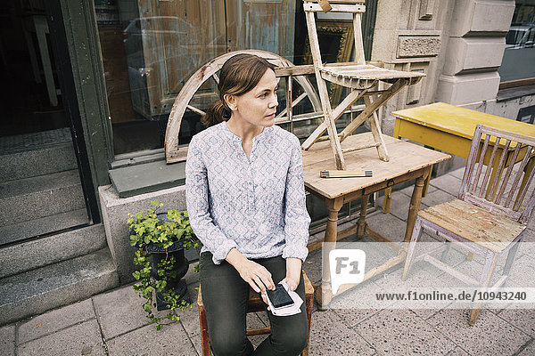 Hochwinkelansicht der Frau mit Smartphone auf Stuhl gegen Laden
