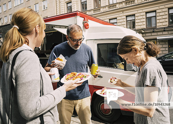 People eating food while standing by truck at city street