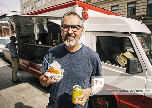 Portrait of happy male customer standing against food truck in city