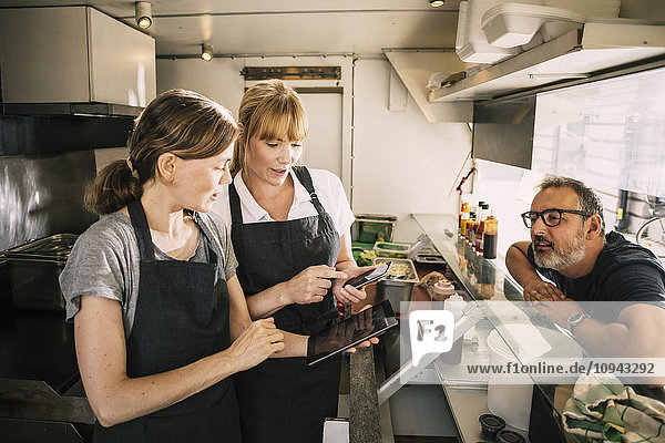 Female chefs with technologies while receiving order from man in food truck