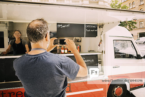 Rear view of owner photographing street food truck in mobile phone
