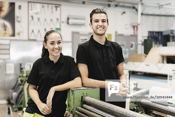 Porträt von lächelnden jungen Gymnasiasten  die in der Werkstatt an Maschinen stehen