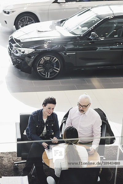 Großer Blickwinkel auf die Unterschriften der Kunden mit dem Autoverkäufer im Showroom