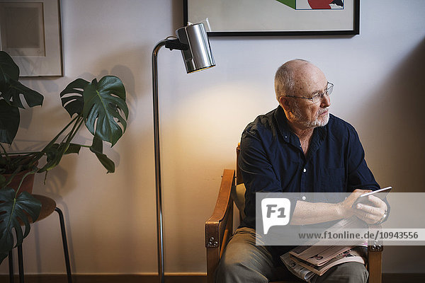 Senior man looking away while holding smart phone at home