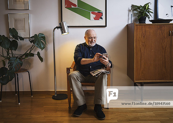 Senior Mann mit Handy auf dem Stuhl zu Hause