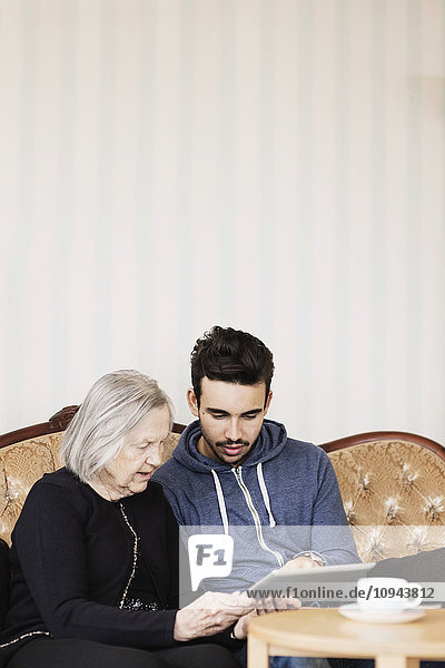 Hausmeisterin und Seniorin mit digitalem Tablett auf dem Sofa im Pflegeheim