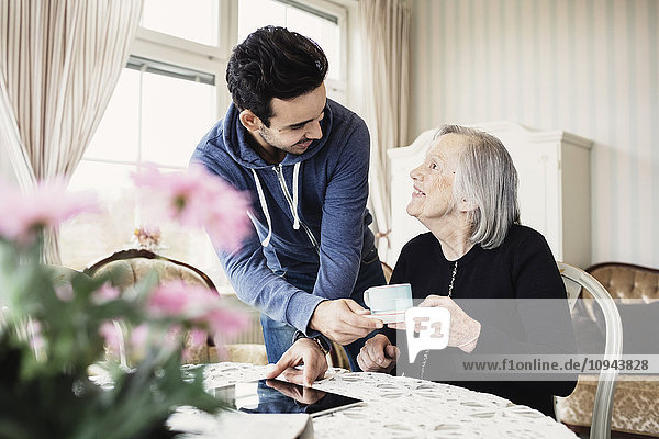 Fröhliche Hausmeisterin serviert Kaffee an Seniorin im Pflegeheim