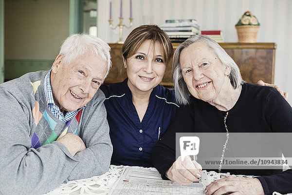Porträt eines lächelnden Hausmeisters und älterer Menschen beim Lösen von Kreuzworträtseln im Pflegeheim