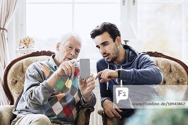 Hausmeisterin unterstützt ältere Männer bei der Nutzung des Mobiltelefons im Pflegeheim
