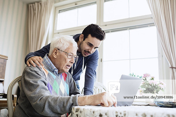 Caretaker and senior man using laptop in nursing home