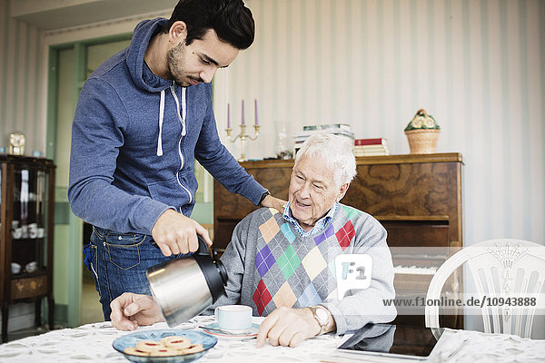 Caretaker serving coffee to senior man at nursing home