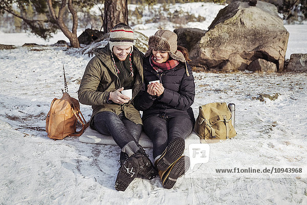 Glückliches Paar beim Kaffeetrinken auf dem schneebedeckten Feld
