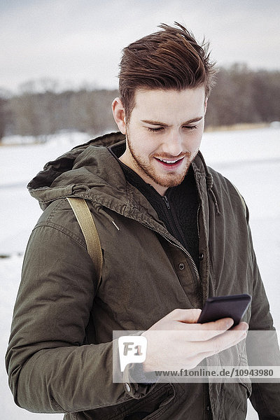 Young man using smart phone while standing on field during winter