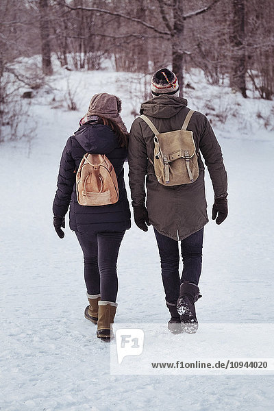 Full length rear view of couple walking on snow covered field