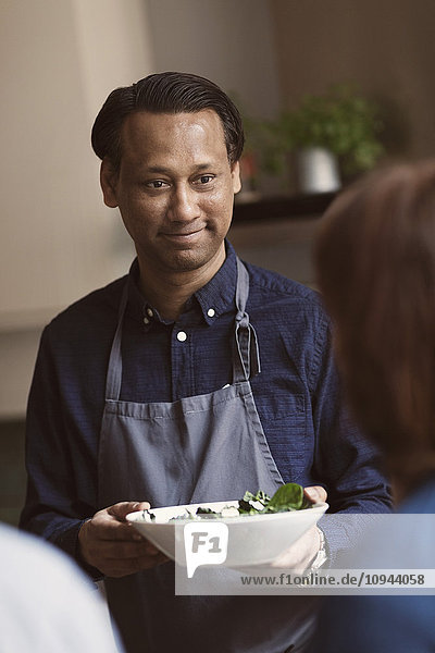Lächelnder reifer Mann hält Salatschüssel  während er eine Freundin ansieht.