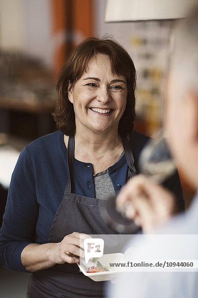 Cheerful woman wearing apron while looking at male friend