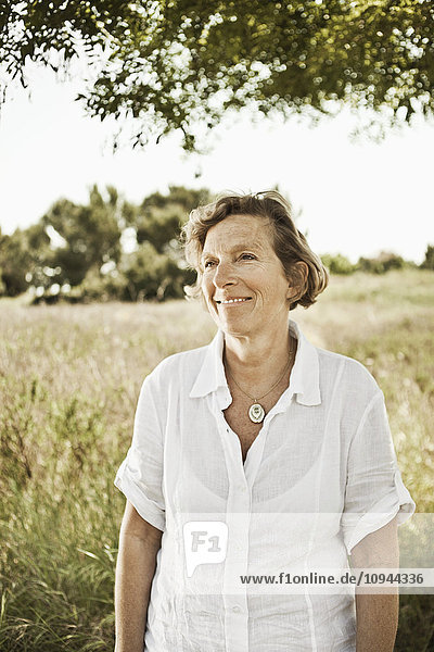 Front view of smiling mature woman standing in grassland
