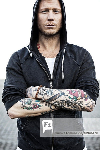 Portrait of a tattooed man in hooded jacket with arms crossed