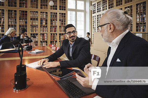 Lächelnder Mann im Gespräch mit dem leitenden Anwalt bei Tisch in der Bibliothek