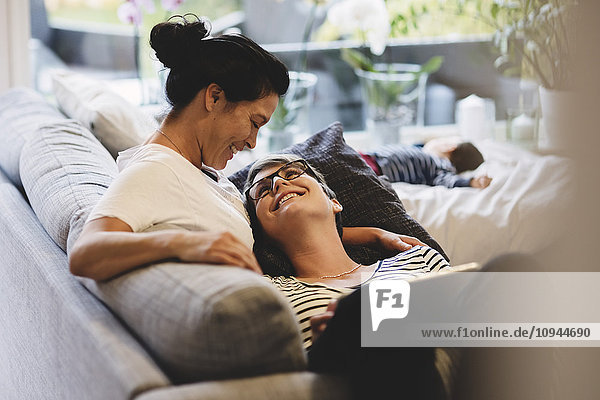 Smiling lesbian couple embracing while baby girl sleeping in living room at home