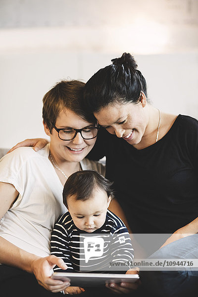 Lächelndes lesbisches Paar und kleines Mädchen  die zu Hause in einem digitalen Tablett suchen.