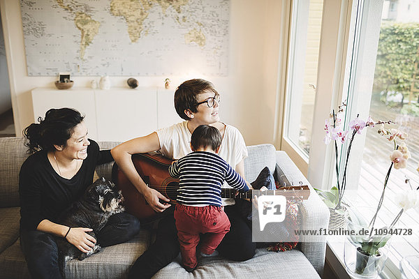 Mother and daughter playing guitar while smiling woman with dog at home