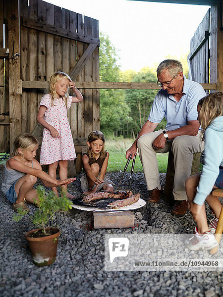 Großvater sitzt mit Kindern zusammen und bedient den Grill