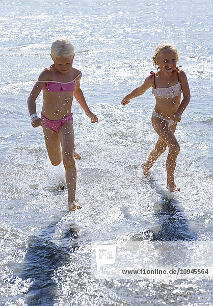 Zwei Mädchen laufen im flachen Wasser