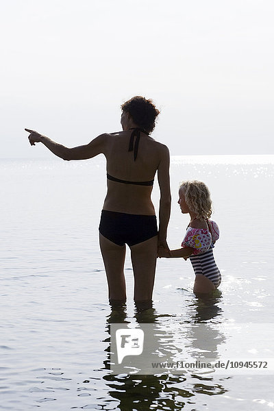 Silhouette of mother and daughter standing in seawater