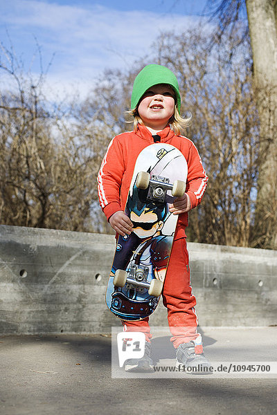 Boy with skateboard standing on sidewalk